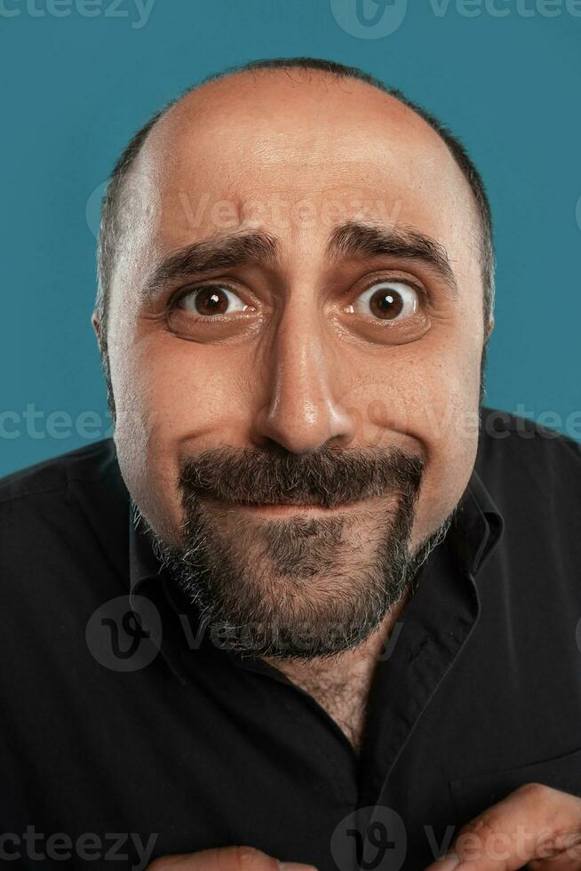 de cerca retrato de un moreno de edad mediana hombre con barba, vestido en un negro camiseta y posando en contra un azul antecedentes. foto