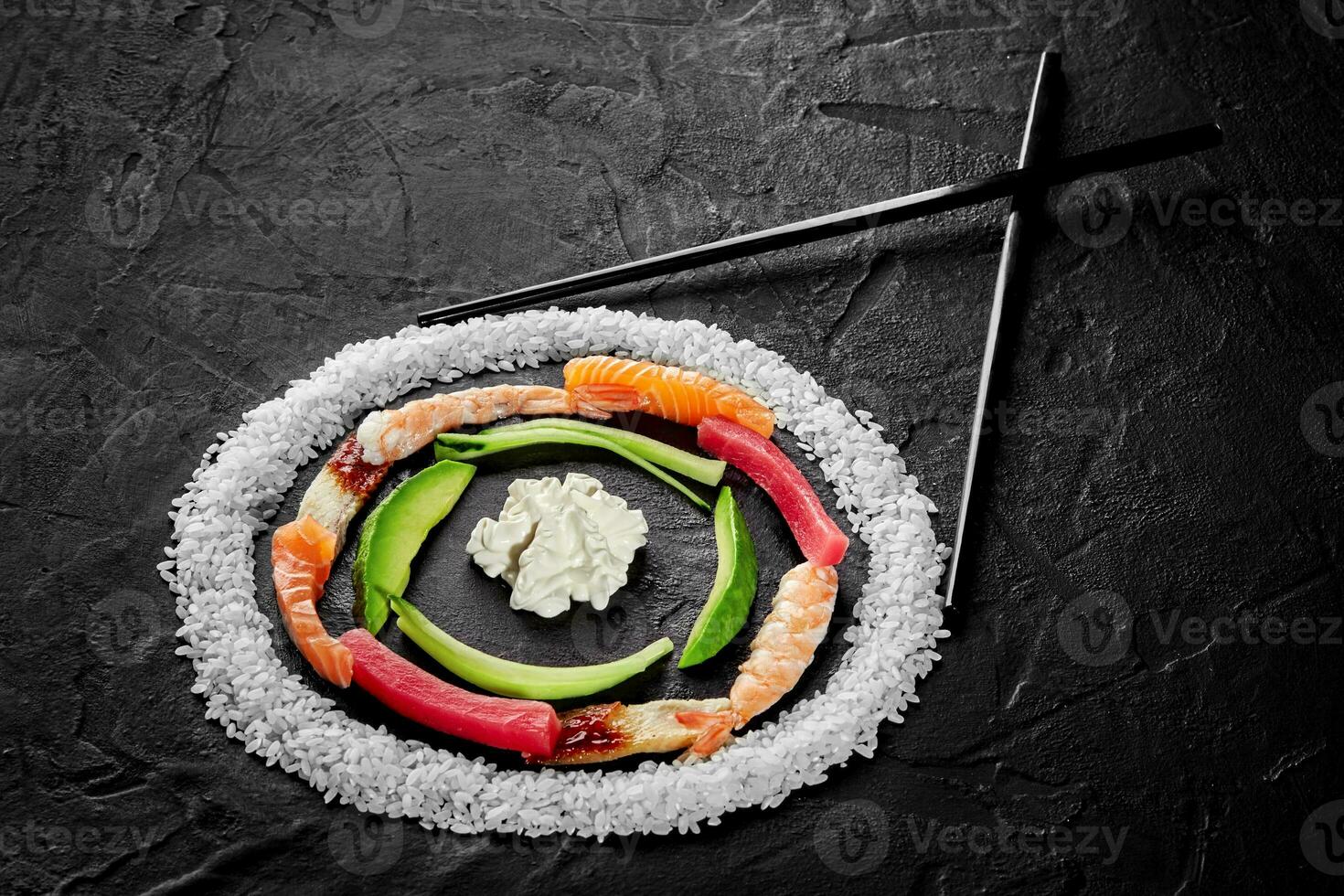 Circle of rice, salmon, eel, tuna and shrimps, avocado and cream cheese with chopsticks on black background photo