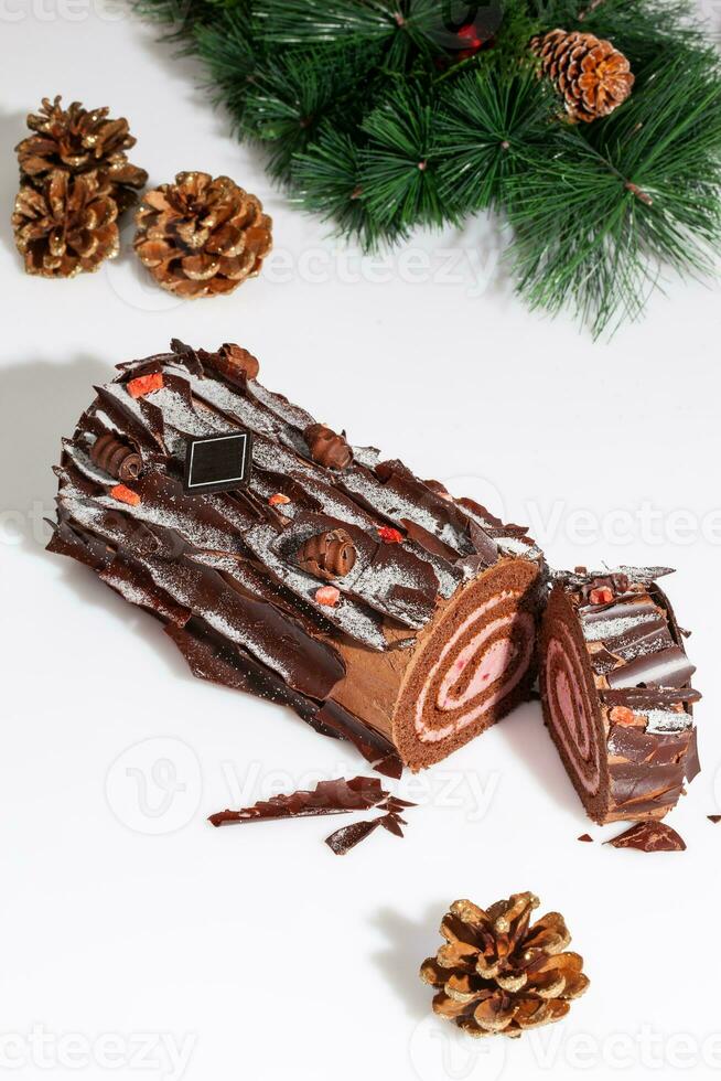 Sliced chocolate roll on white background with pine branch and fir cones photo