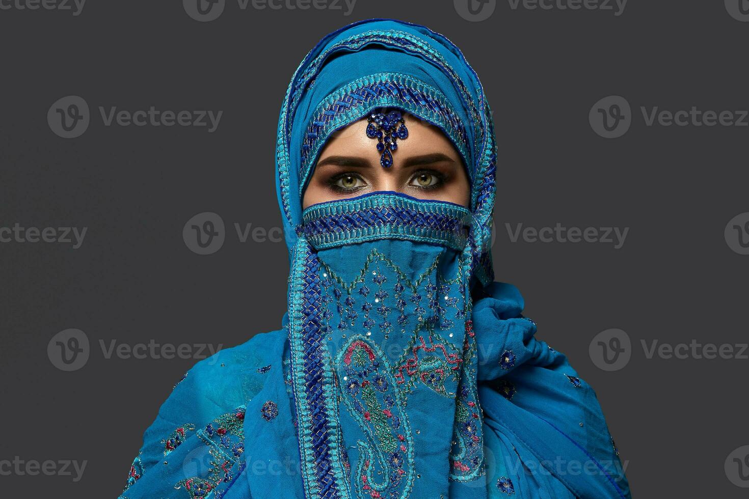 Studio shot of a young beautiful woman wearing the blue hijab decorated with sequins and jewelry. Arabic style. photo