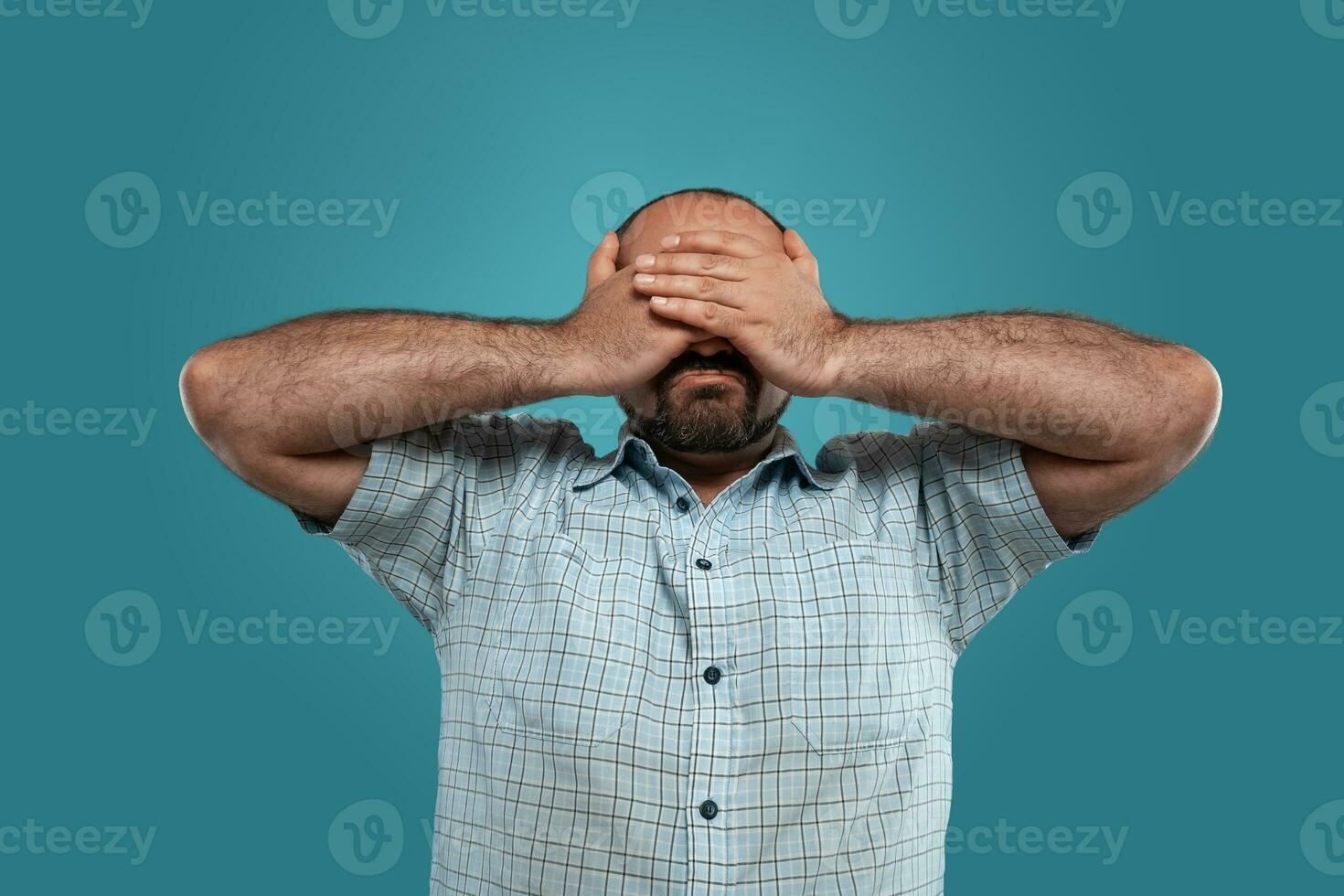 Close-up portrait of a brunet middle-aged man with beard, dressed in a light checkered shirt and posing against a blue background. photo