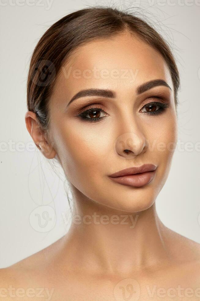 Close up portrait of a brunette nude model girl with professional evening make-up and plump lips, posing on gray background. photo