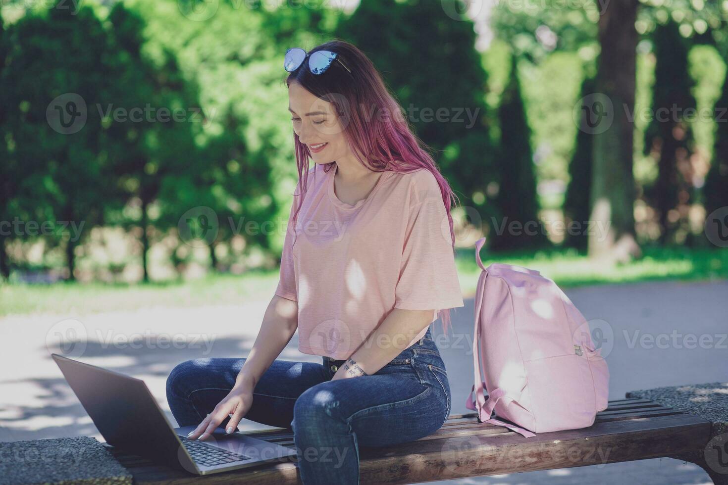 joven niña es estudiando en el primavera parque, sentado en el de madera foto