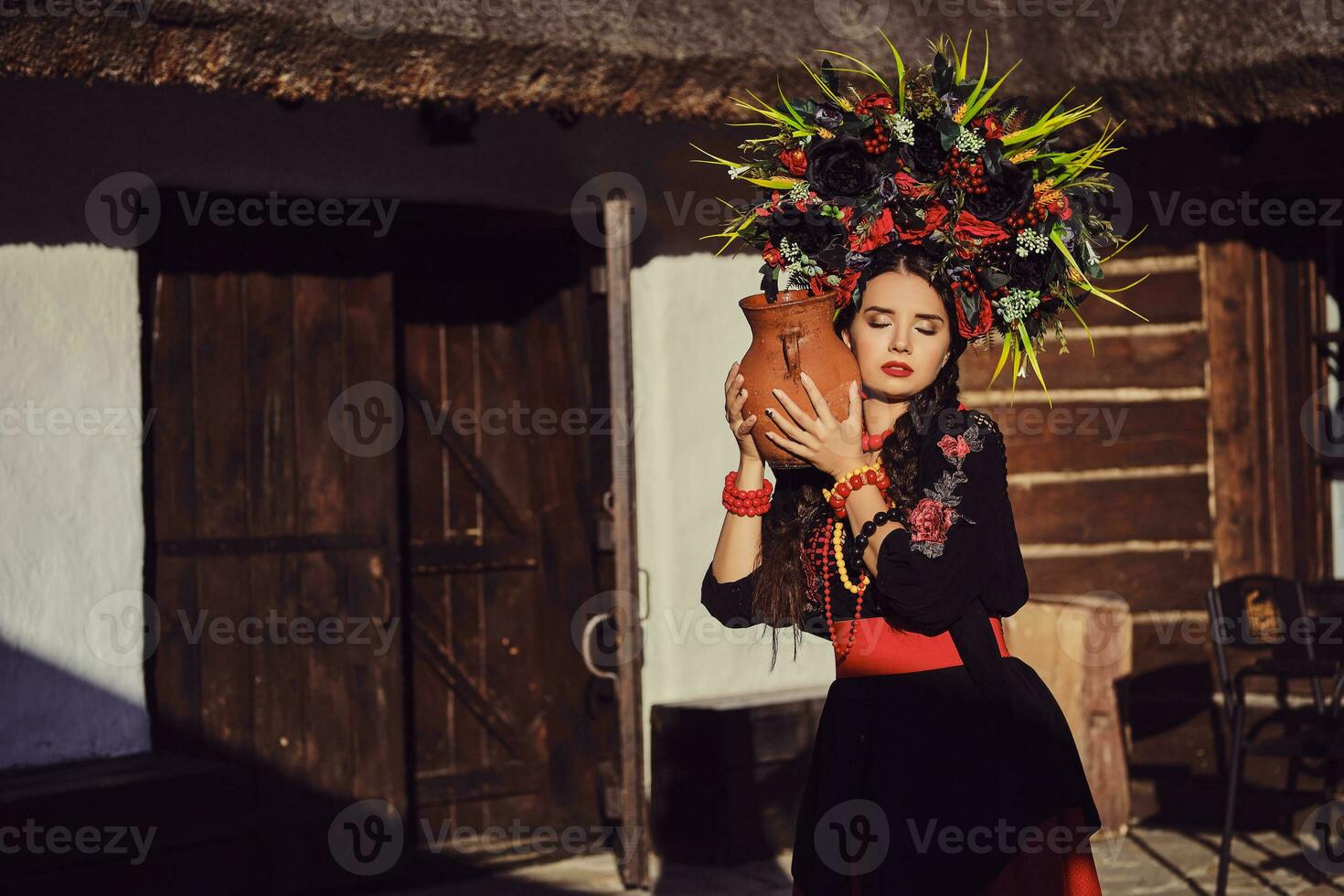 Brunette girl in a black and red ukrainian embroidered authentic national costume and a wreath of flowers is posing standing at the gate. photo