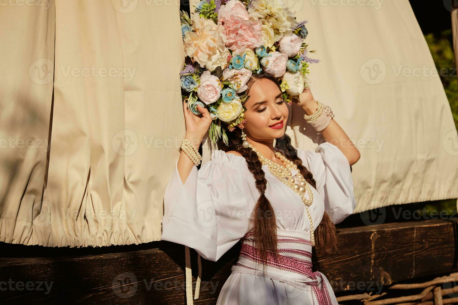 Brunette girl in a white ukrainian authentic national costume and a wreath of flowers is posing against a terrace. Close-up. photo