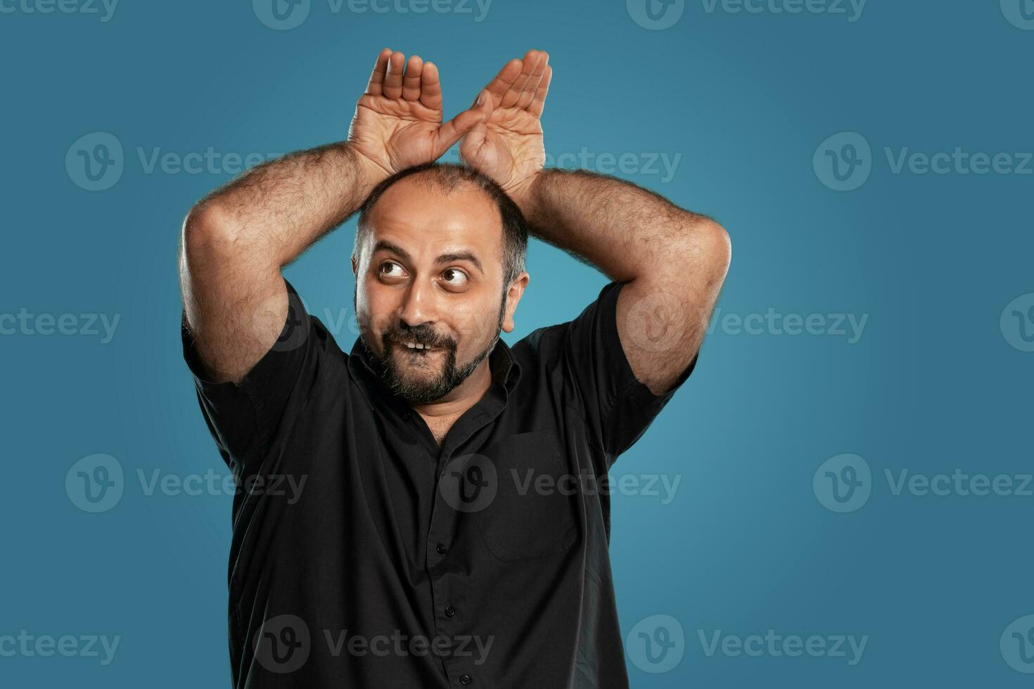 Close-up portrait of a brunet middle-aged man with beard, dressed in a black t-shirt and posing against a blue background. photo