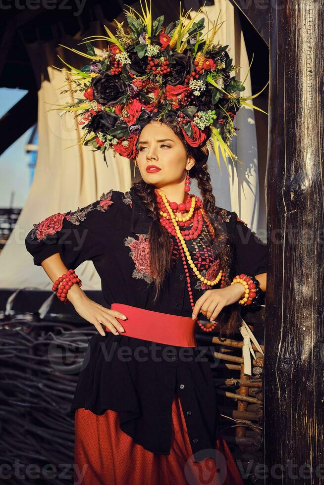 Brunette girl in a white ukrainian authentic national costume and a wreath of flowers is posing against a terrace. Close-up. photo