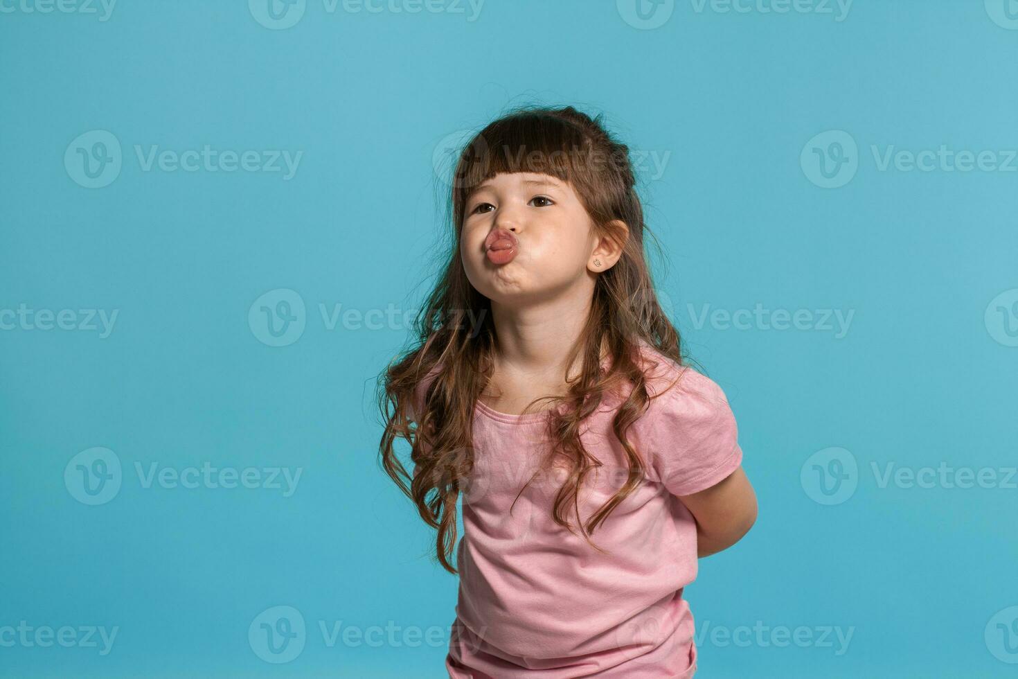 Beautiful little girl wearing in a pink t-shirt is posing against a blue studio background. photo