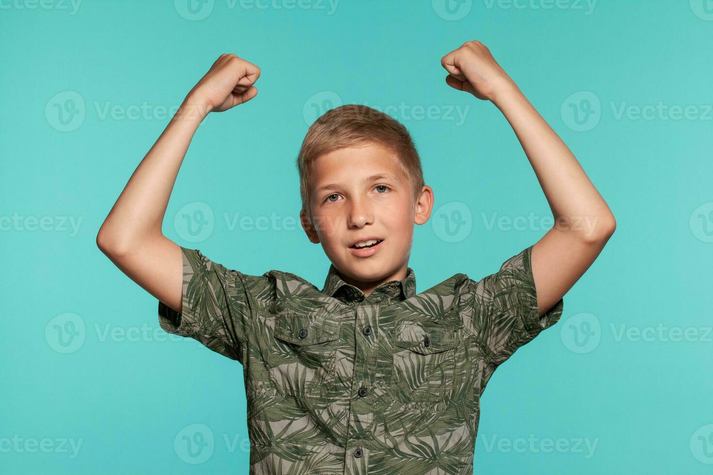 Close-up portrait of a blonde teenage boy in a green shirt with palm print posing against a blue studio background. Concept of sincere emotions. photo