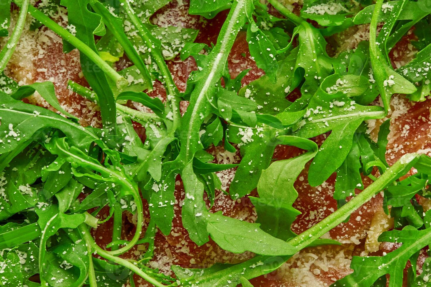 Closeup of arugula leaves on prosciutto slices sprinkled with grated parmesan on pizza photo