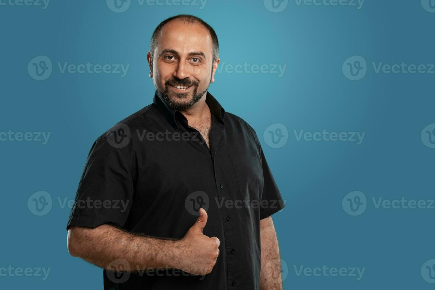 Close-up portrait of a brunet middle-aged man with beard, dressed in a black t-shirt and posing against a blue background. photo