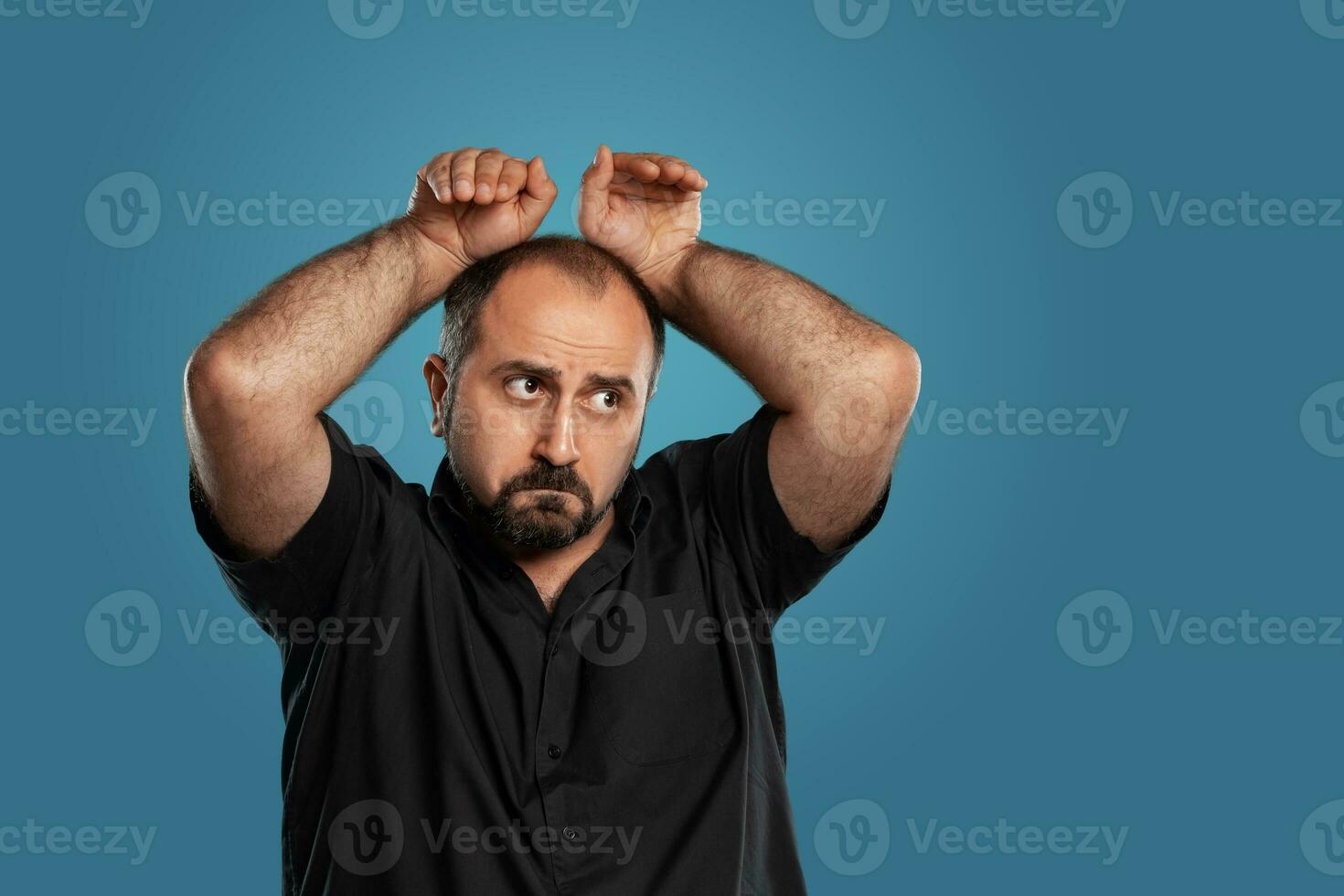 Close-up portrait of a brunet middle-aged man with beard, dressed in a black t-shirt and posing against a blue background. photo