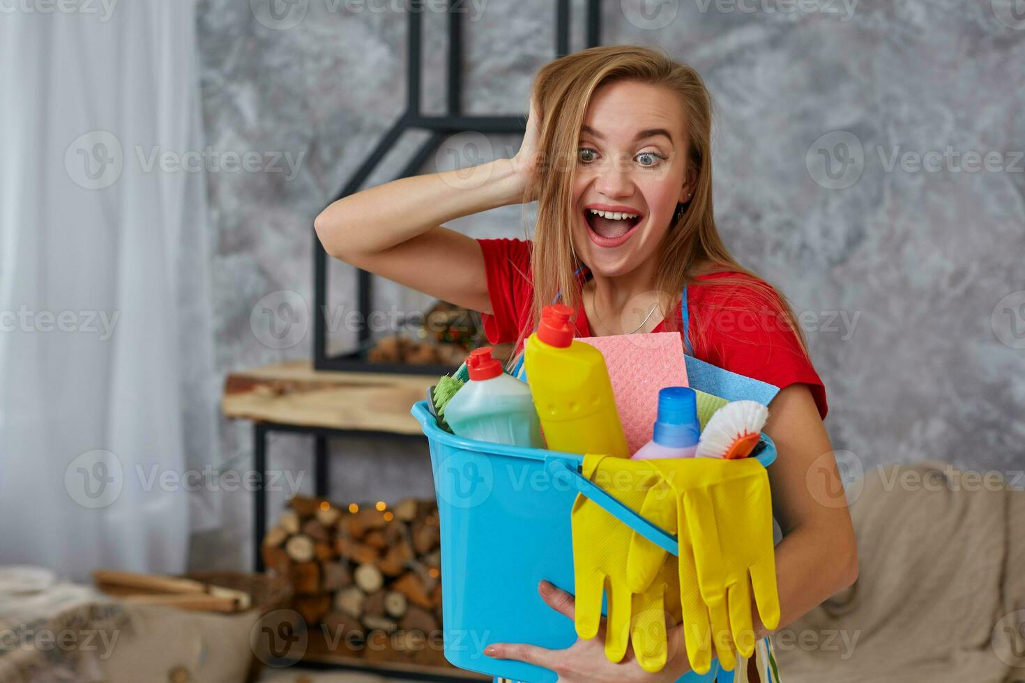 A cleaning woman is standing in living room holding a blue bucket fulfilled with chemicals and facilities for tidying up in her hand photo