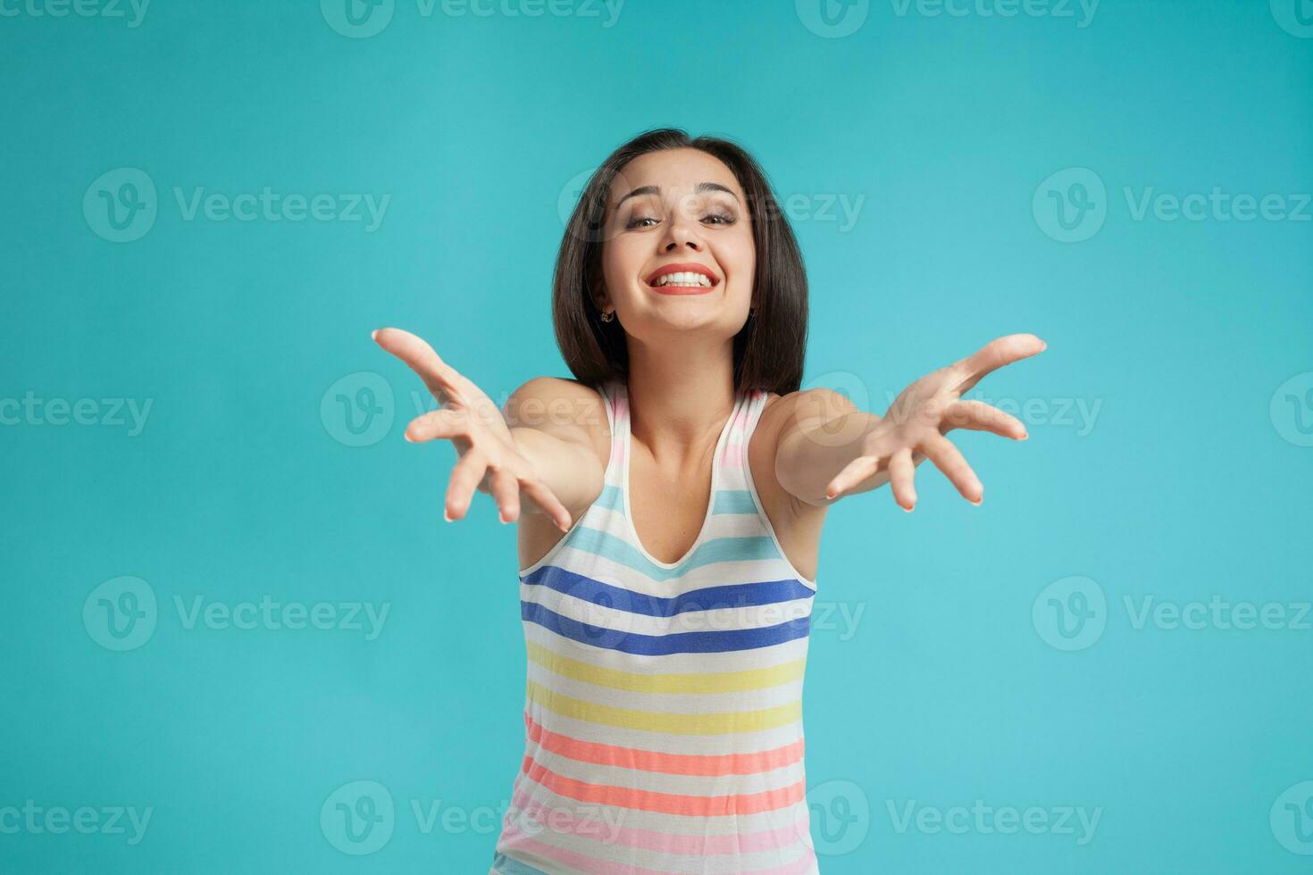 Brunette woman with long hair, dressed in colorful striped shirt, posing against blue studio background. Sincere emotions. Close-up. photo