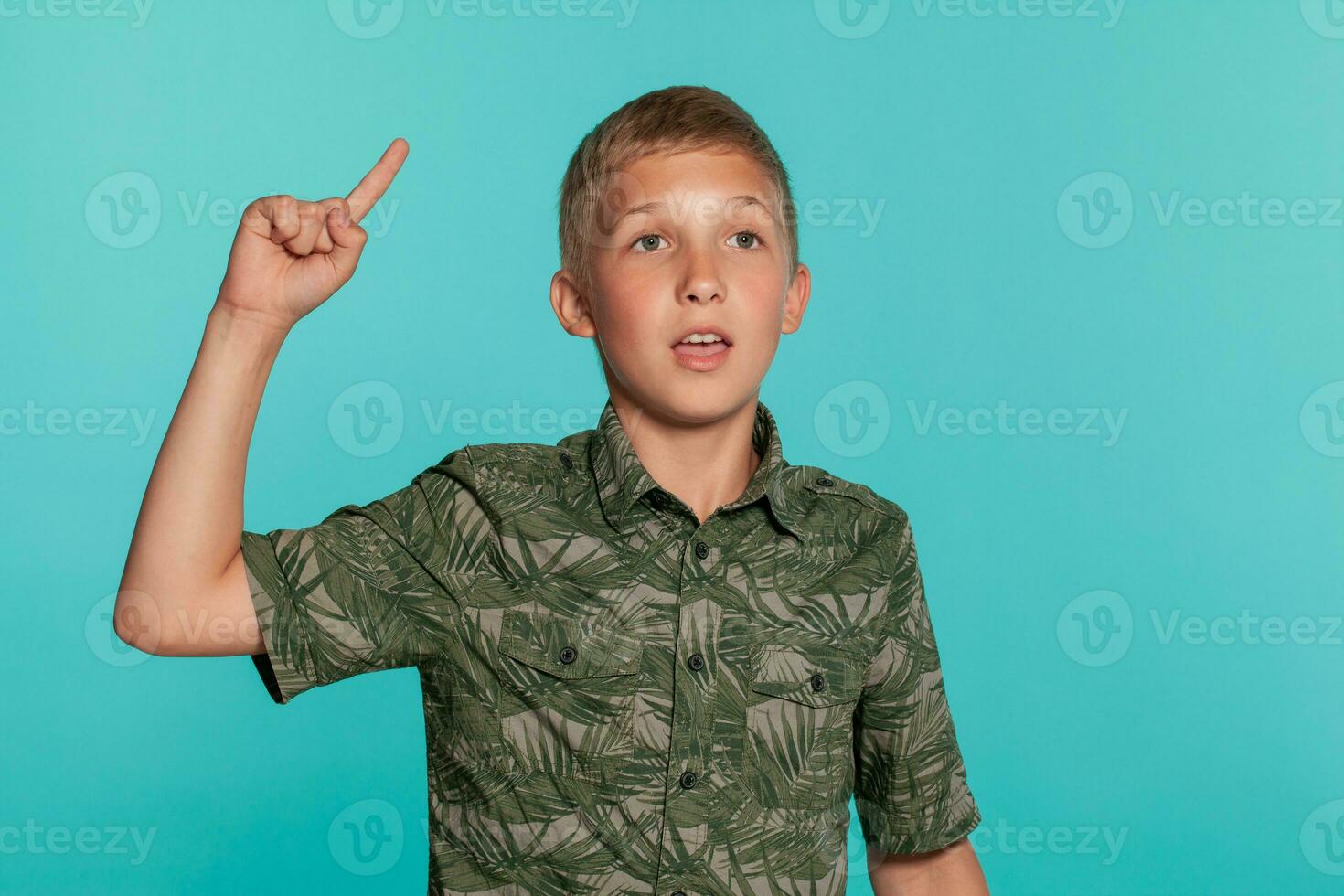 Close-up portrait of a blonde teenage boy in a green shirt with palm print posing against a blue studio background. Concept of sincere emotions. photo