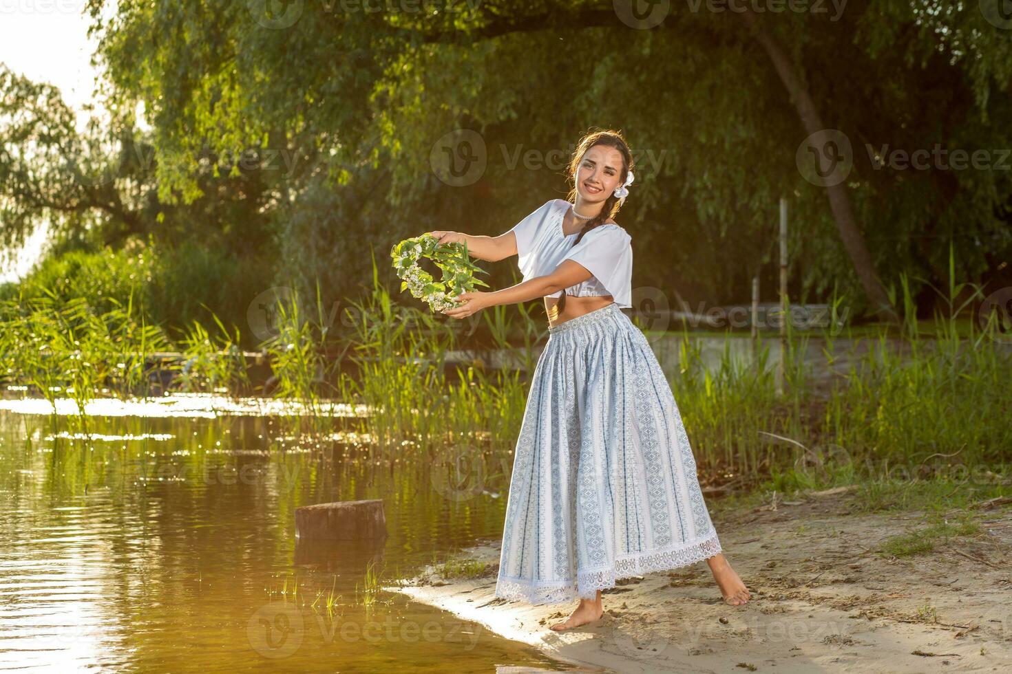 Young beautiful caucasian woman standing at the bank of river. Traditional countryside picture with girl at foreground and copy space. Sun flare photo