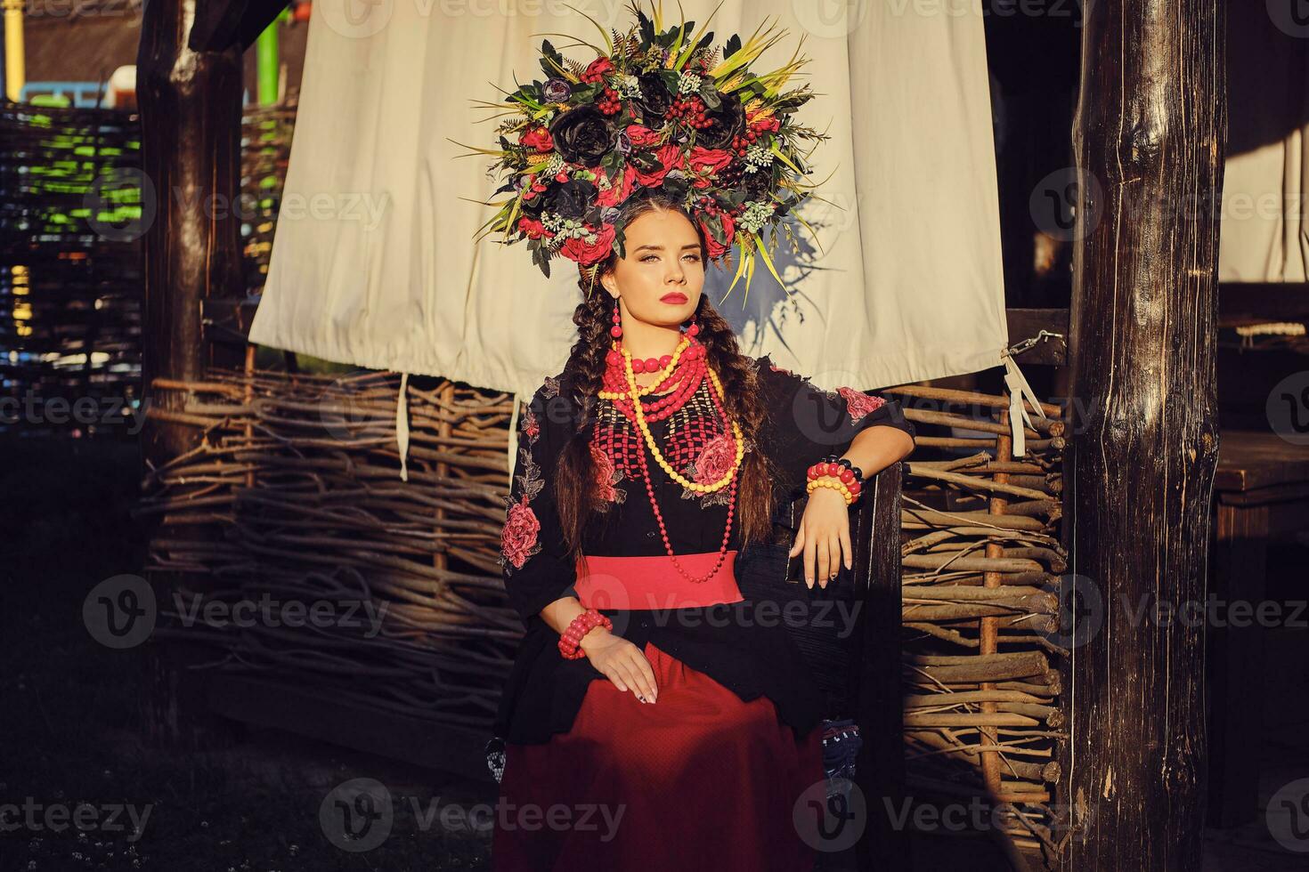 Brunette girl in a black and red embroidered ukrainian authentic national costume and a wreath of flowers is posing against a terrace. Close-up. photo