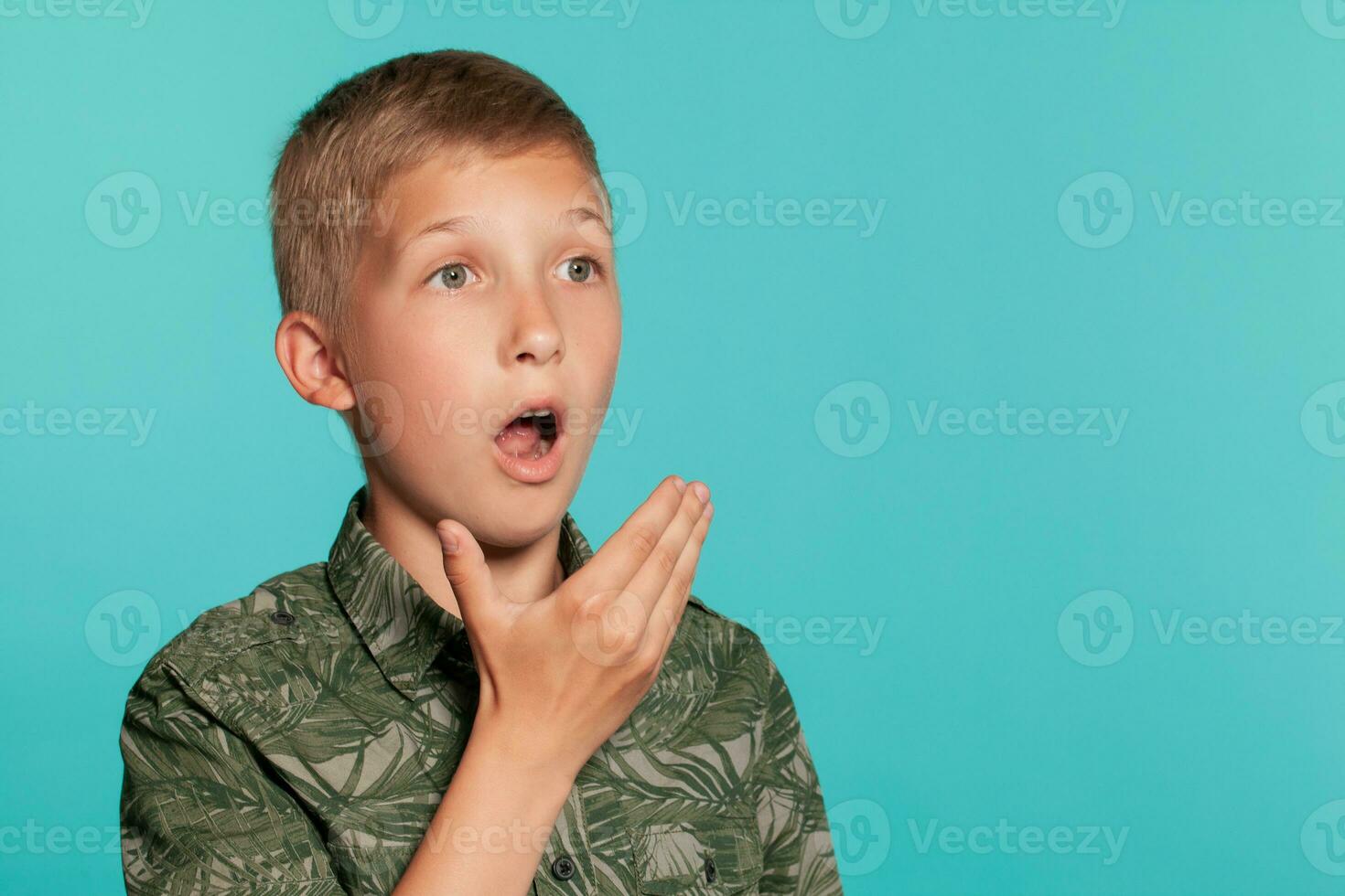 Close-up portrait of a blonde teenage boy in a green shirt with palm print posing against a blue studio background. Concept of sincere emotions. photo