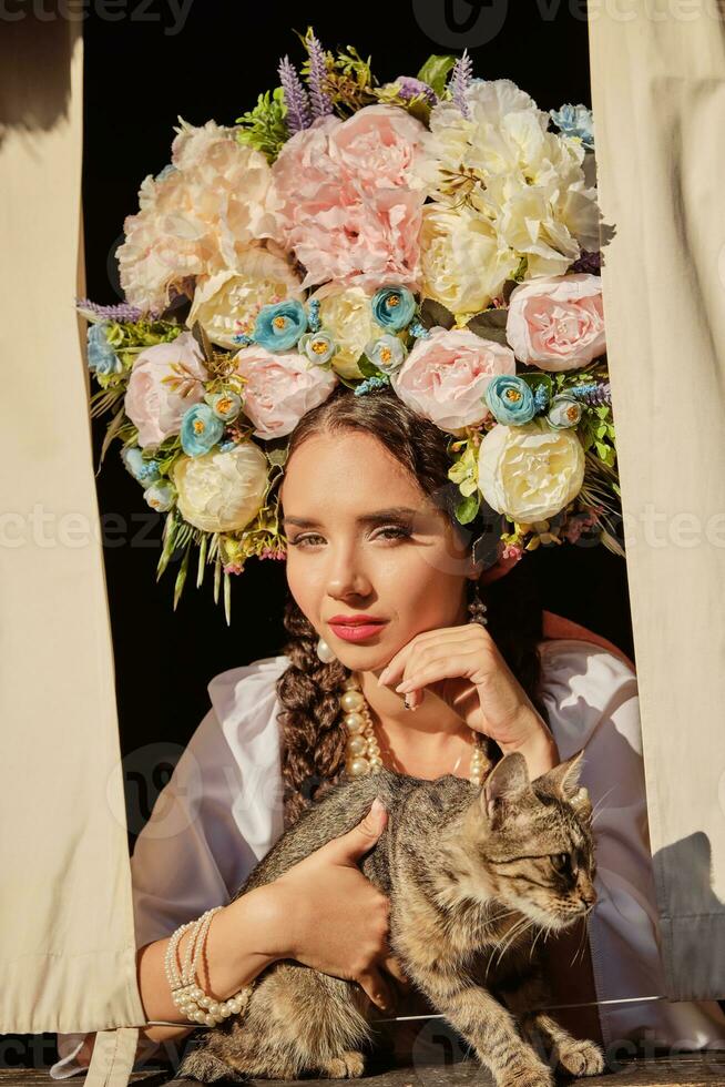 Brunette girl in a white ukrainian authentic national costume and a wreath of flowers is is looking out of the window. Close-up. photo