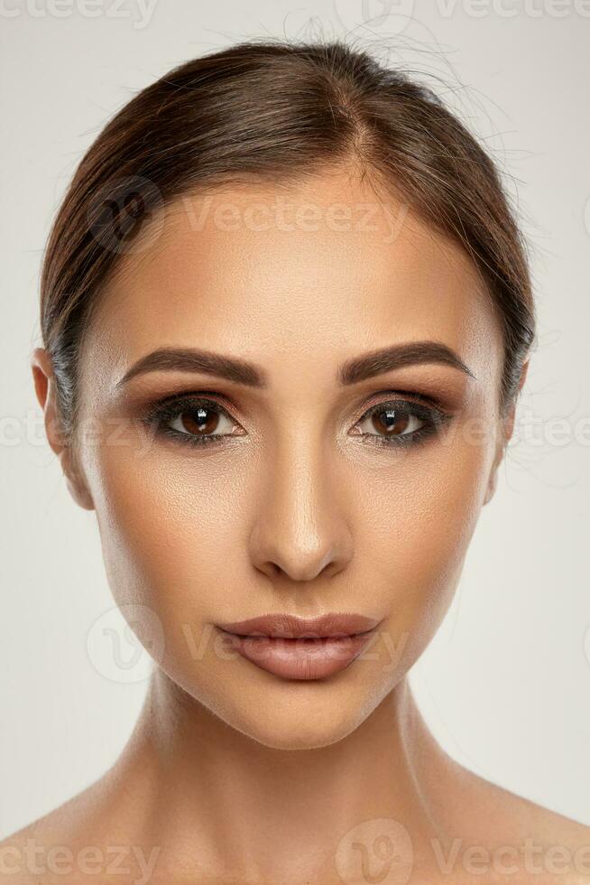 Close up portrait of a brunette nude model girl with professional evening make-up and plump lips, posing on gray background. photo