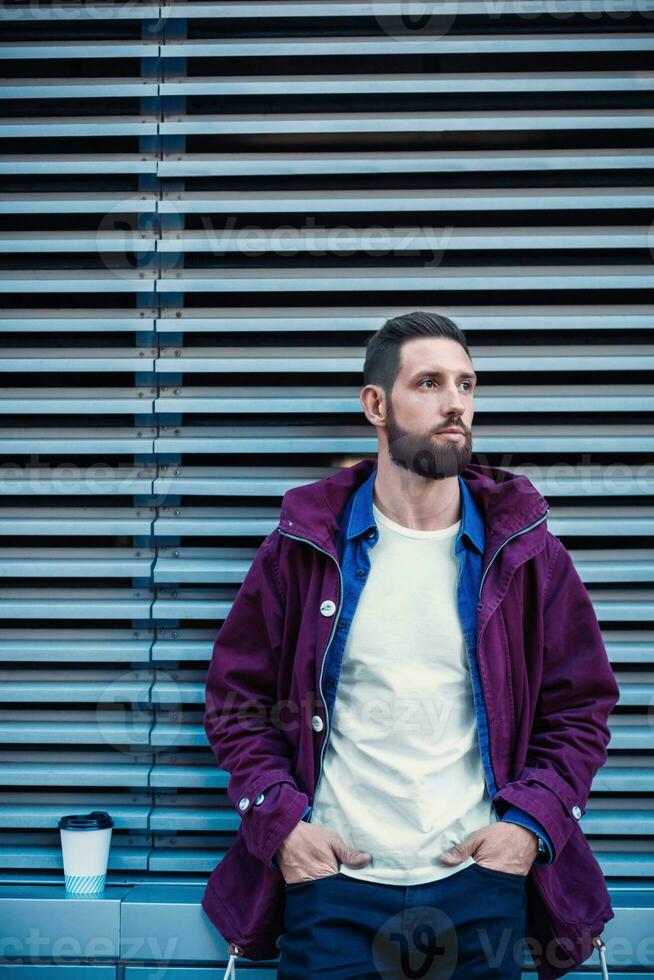 Handsome young man in purple winter jacket drinking coffee. The guy drinking coffee on the street. photo