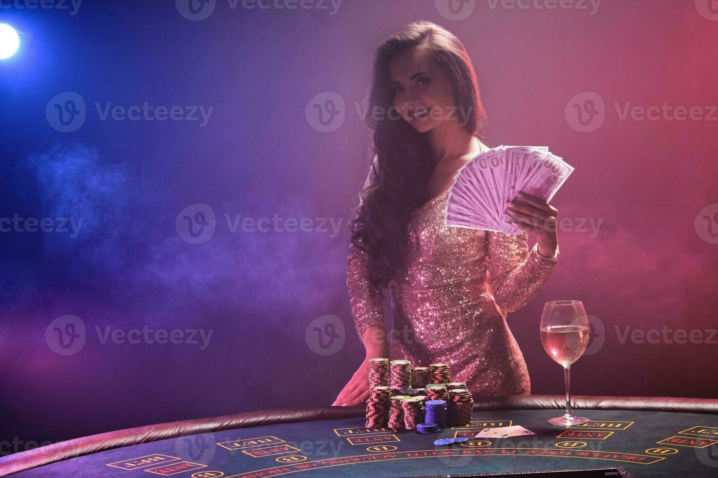 morena niña con un Perfecto peinado y brillante maquillaje es posando con ventilador de cien dólar cuentas en su manos. casino, póker. foto