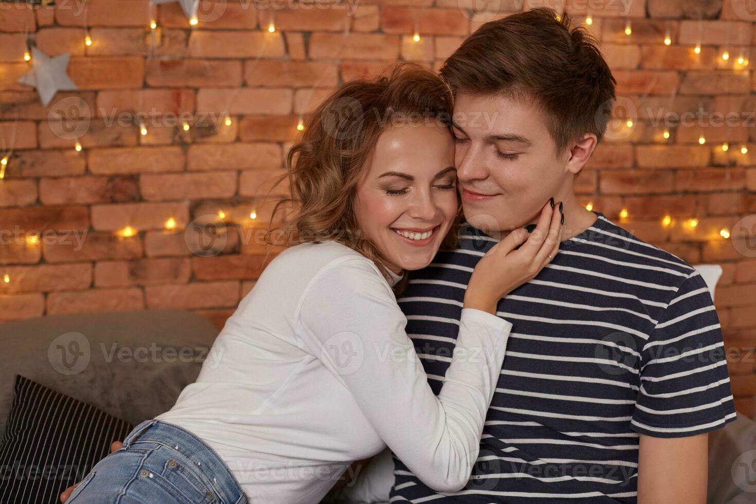 Happy loving couple relaxing on bed at home, young woman touching smiling handsome man face photo