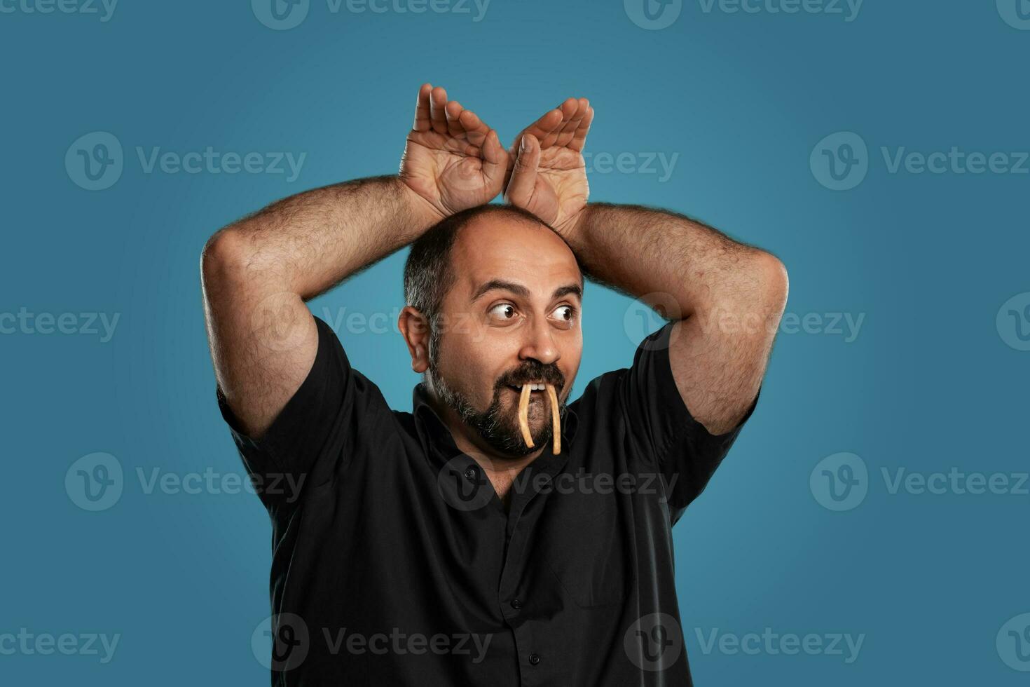 Close-up portrait of a brunet middle-aged man with beard, dressed in a black t-shirt and posing against a blue background. photo