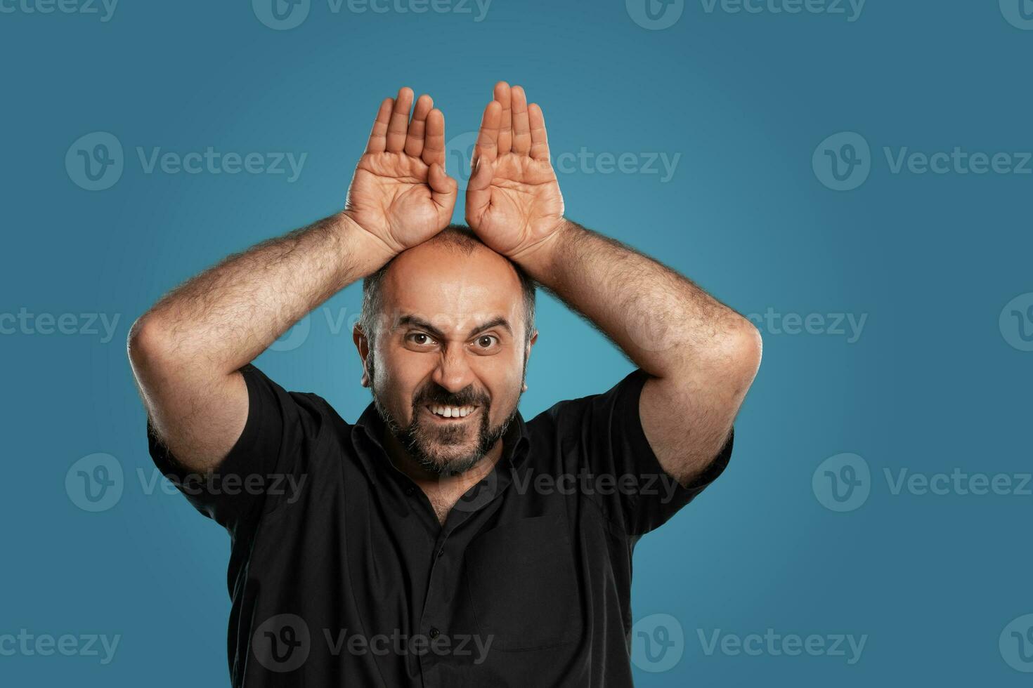 Close-up portrait of a brunet middle-aged man with beard, dressed in a black t-shirt and posing against a blue background. photo