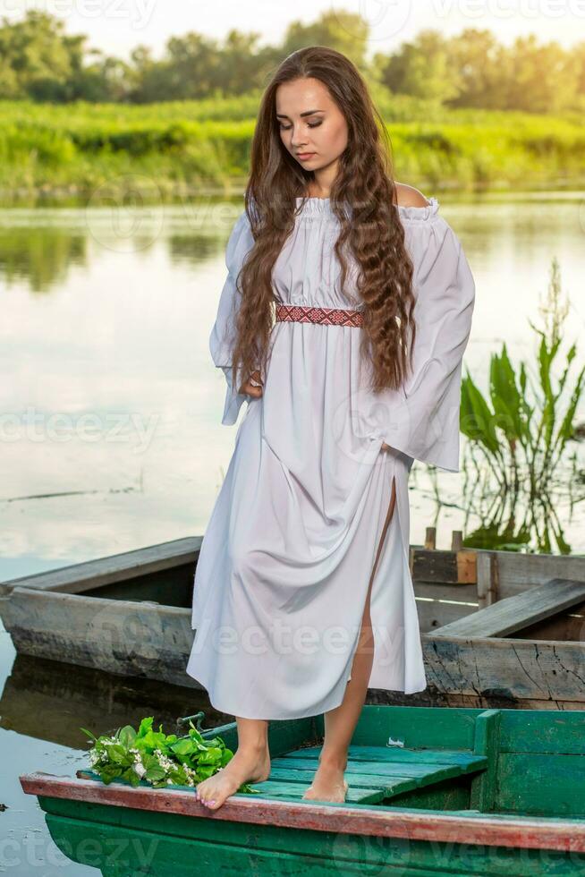 Young sexy woman on boat at sunset. The girl has a flower wreath on her head, relaxing and sailing on river. Fantasy art photography. photo