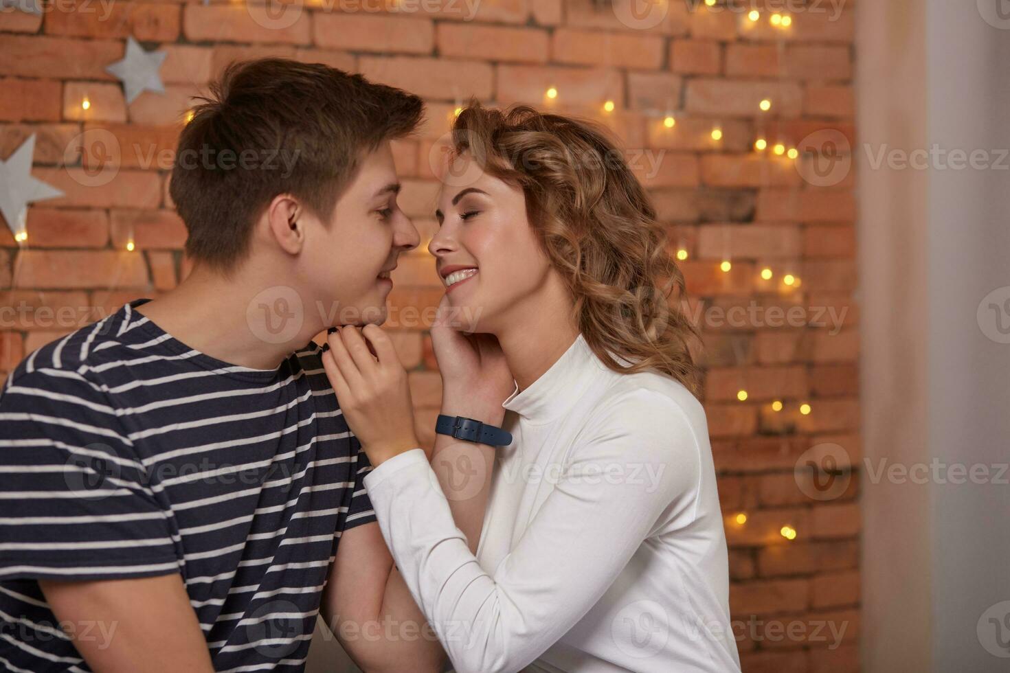 Happy loving couple relaxing on bed at home, young man touching smiling beautiful woman face, looking in the eyes. photo