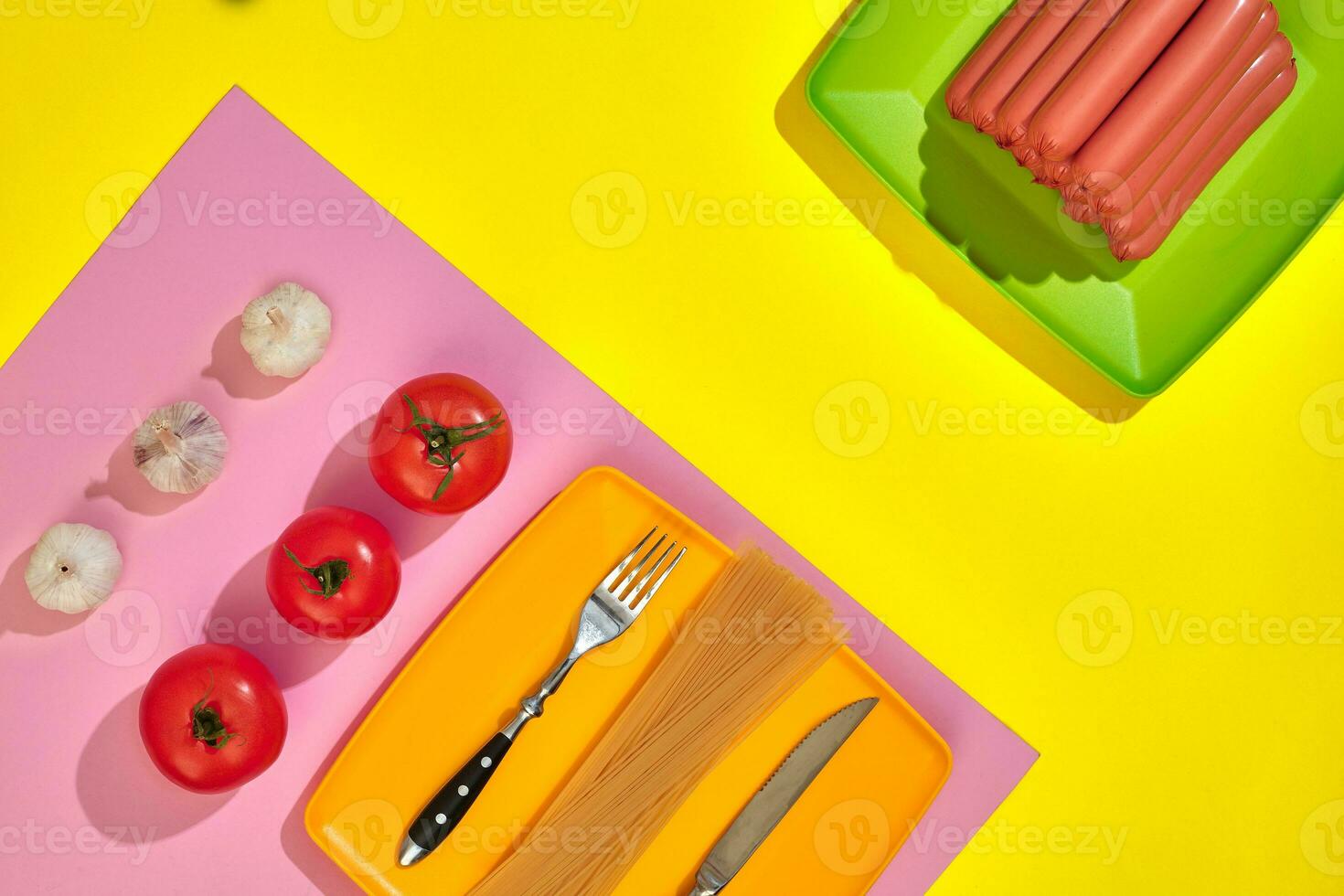 A lot of raw sausages on plate. On yellow background with pasta and vegetables, top view. photo