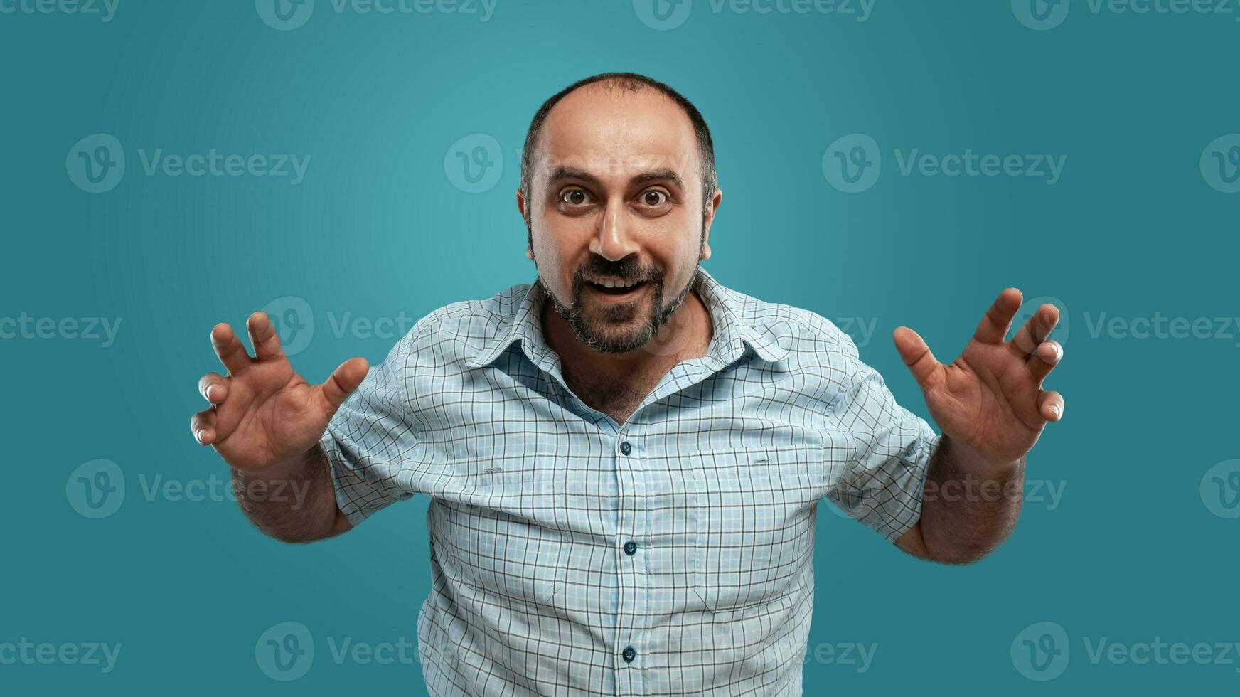 Close-up portrait of a brunet middle-aged man with beard, dressed in a light checkered shirt and posing against a blue background. photo