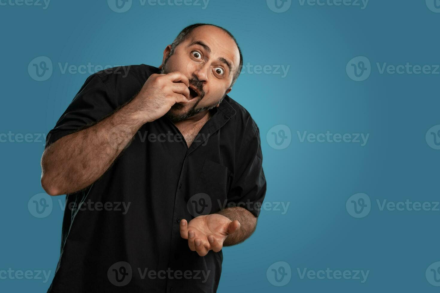 Close-up portrait of a brunet middle-aged man with beard, dressed in a black t-shirt and posing against a blue background. photo