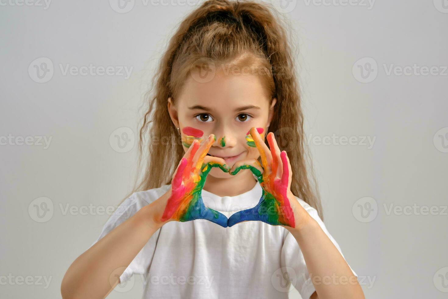 Little girl in white t-shirt is posing standing isolated on white and gesticulating with her painted in different colors palms. Art studio. Close-up. photo