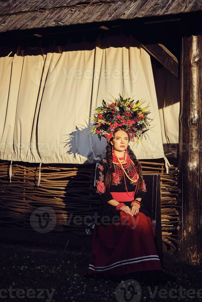 morena niña en un negro y rojo bordado ucranio auténtico nacional disfraz y un guirnalda de flores es posando en contra un terraza. de cerca. foto