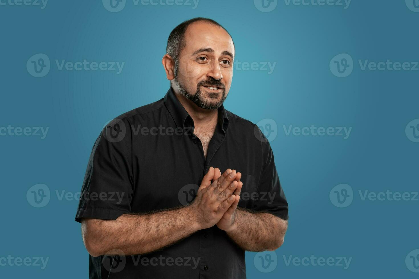 Close-up portrait of a brunet middle-aged man with beard, dressed in a black t-shirt and posing against a blue background. photo