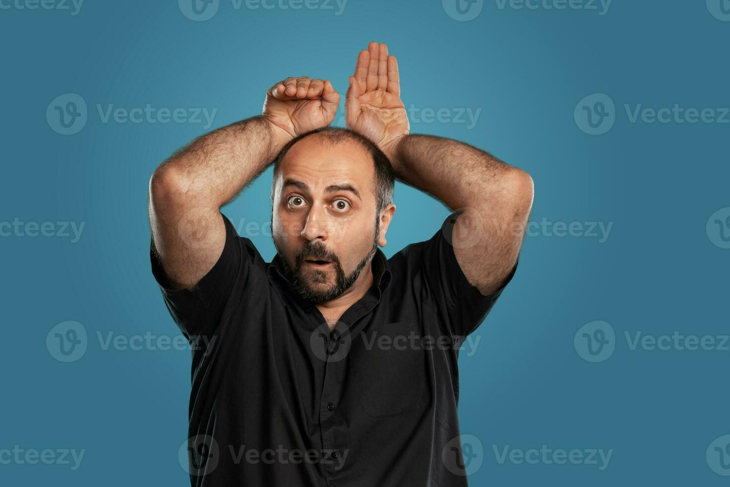 Close-up portrait of a brunet middle-aged man with beard, dressed in a black t-shirt and posing against a blue background. photo