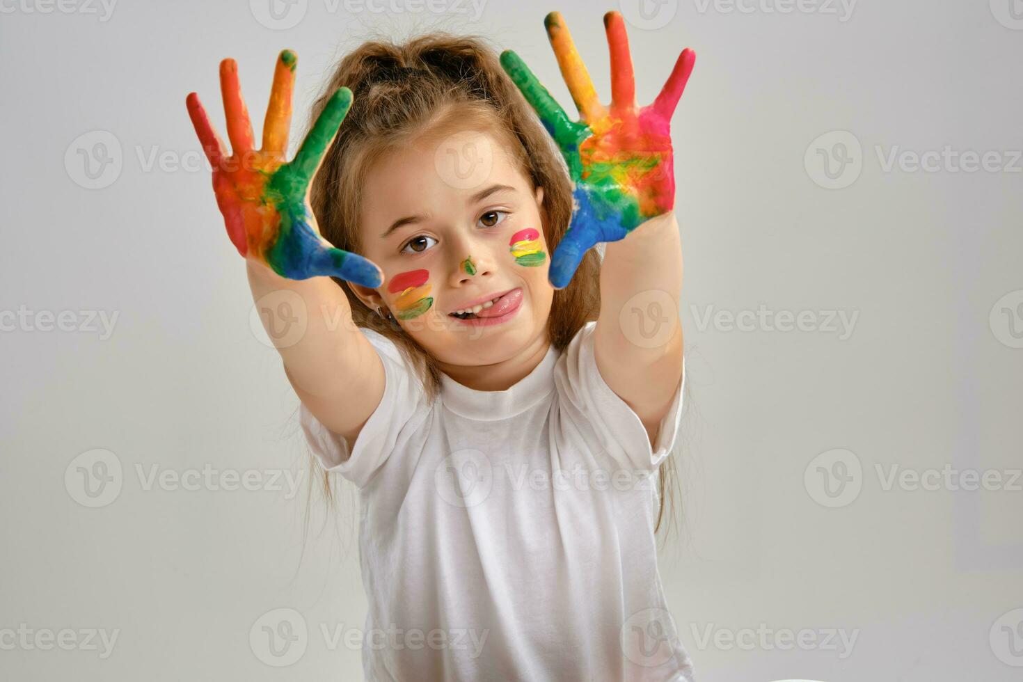 Little girl in white t-shirt is posing standing isolated on white and showing her painted hands, face. Art studio. Close-up. photo