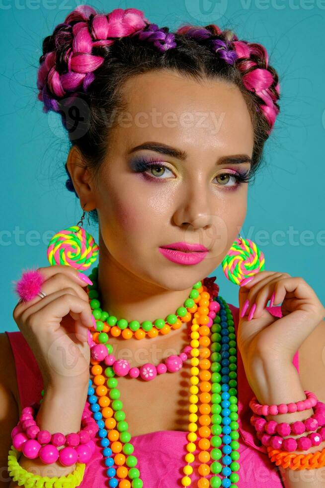 Lovely girl with a multi-colored braids hairstyle and bright make-up, posing in studio against a blue background. photo