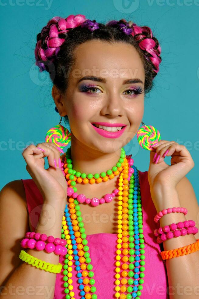 Lovely girl with a multi-colored braids hairstyle and bright make-up, posing in studio against a blue background. photo