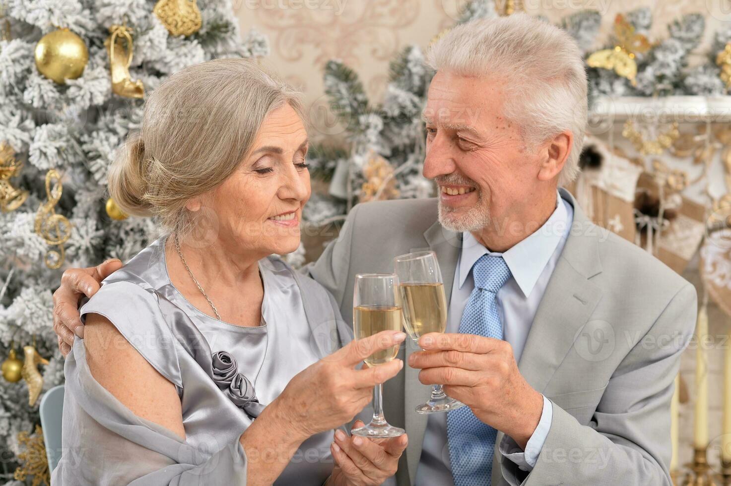 Old couple with champagne celebrating Christmas near tree photo