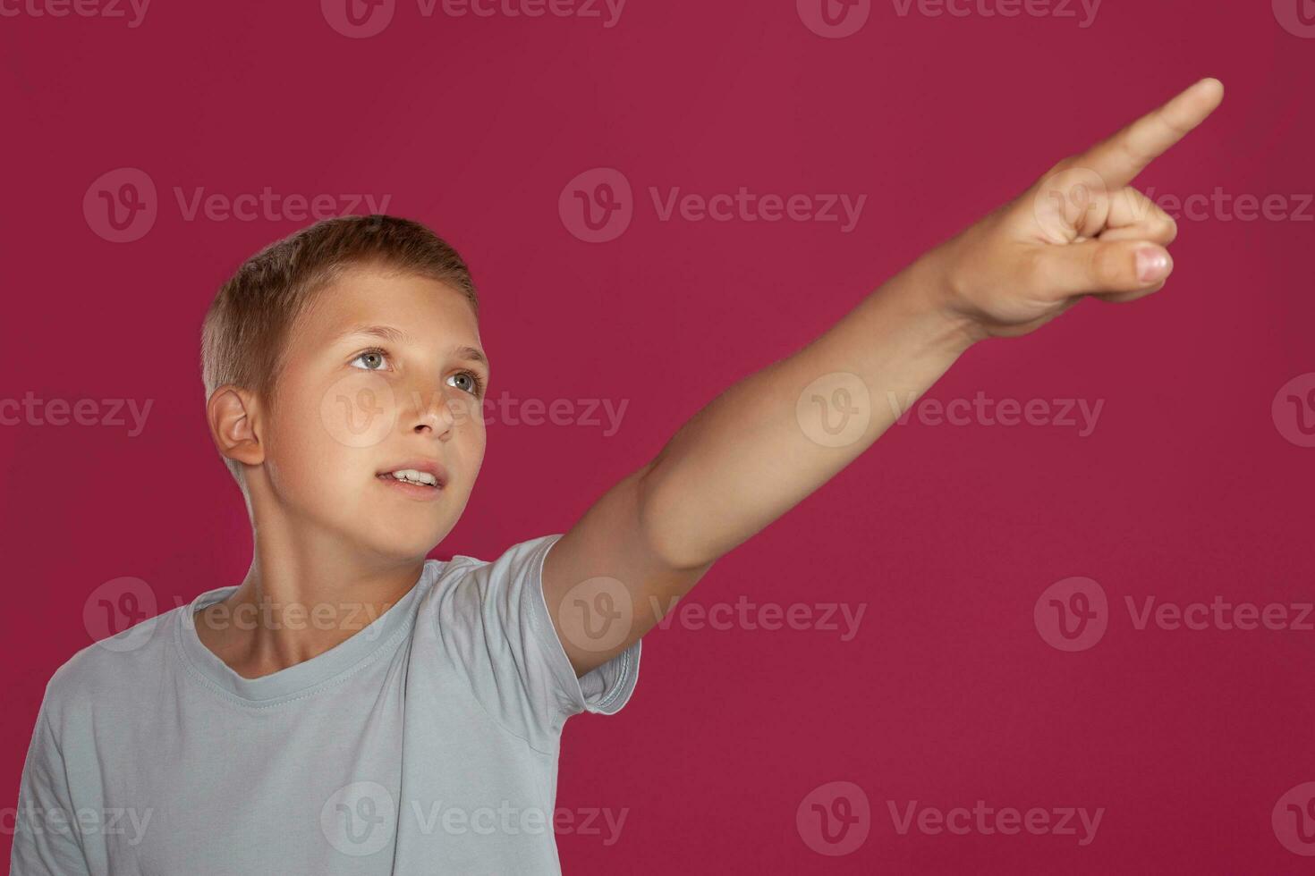 Close-up portrait of a blonde teenage boy in a white t-shirt posing against a pink studio background. Concept of sincere emotions. photo