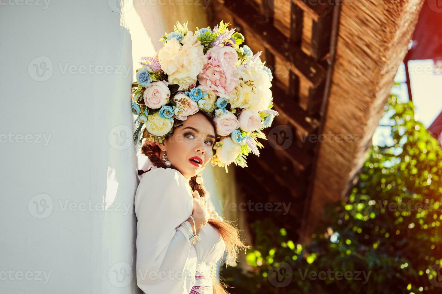 morena niña en un blanco ucranio auténtico nacional disfraz y un guirnalda de flores es posando en contra un blanco cabaña. foto