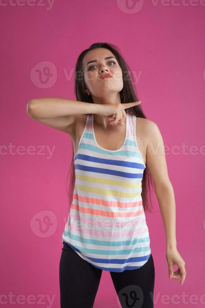 Brunette woman with long hair, dressed in colorful striped shirt, posing against pink studio background. Sincere emotions. Close-up. photo