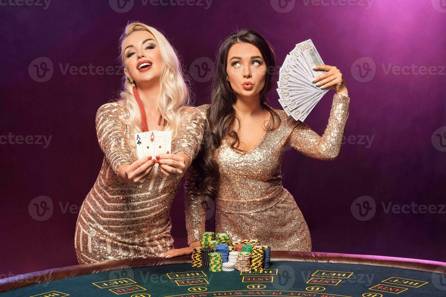 Beautiful girls with a perfect hairstyles and bright make-up are posing standing at a gambling table. Casino, poker. photo