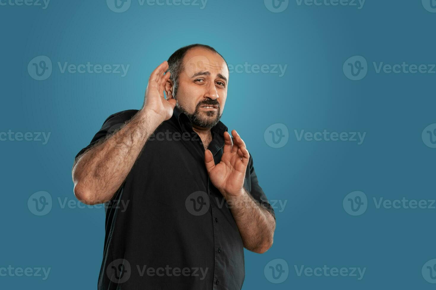 de cerca retrato de un moreno de edad mediana hombre con barba, vestido en un negro camiseta y posando en contra un azul antecedentes. foto