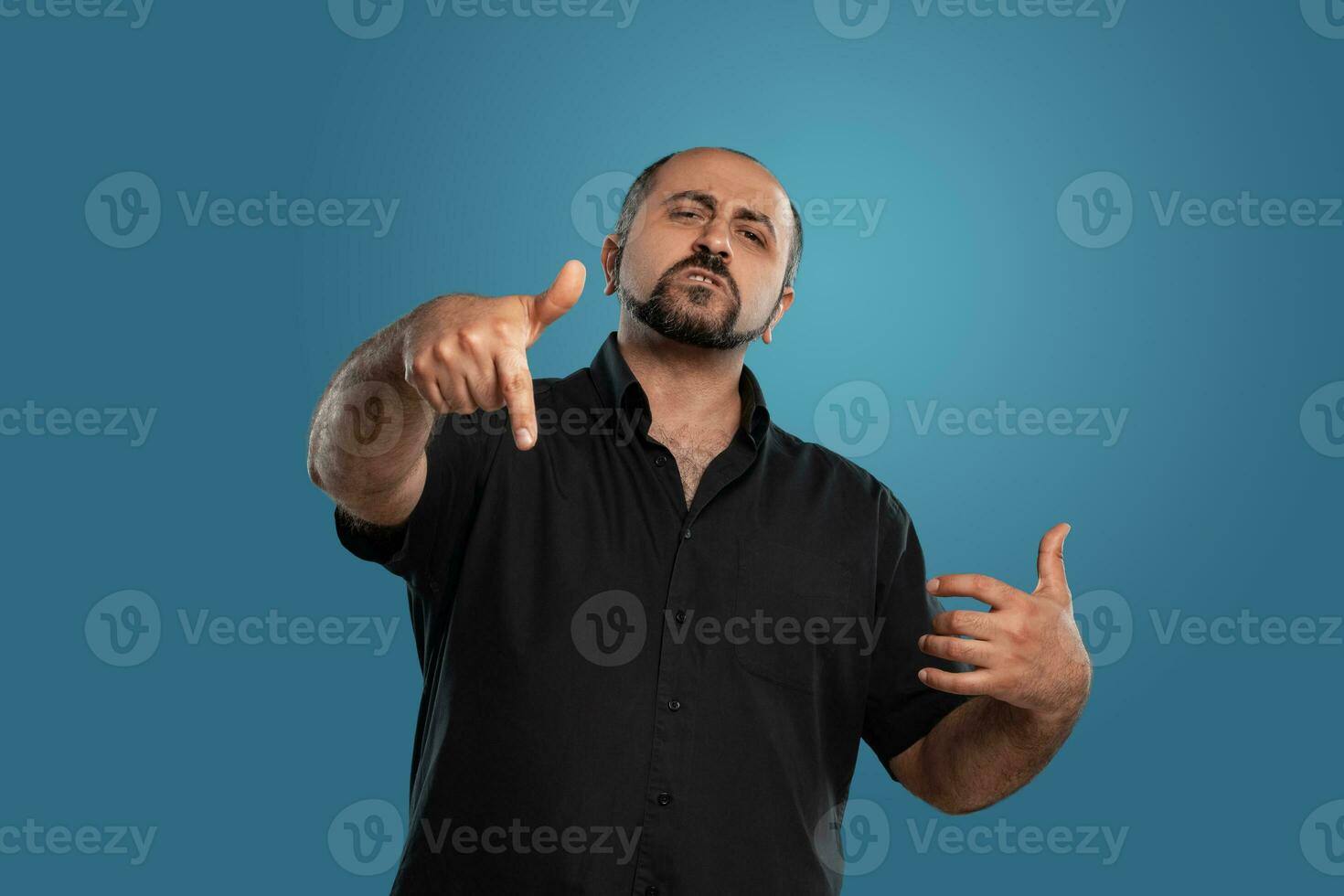 de cerca retrato de un moreno de edad mediana hombre con barba, vestido en un negro camiseta y posando en contra un azul antecedentes. foto