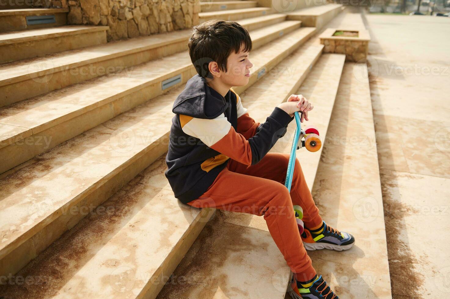 Teenage student boy, schoolboy in sportswear sitting on steps in urban skatepark, thoughtfully looking into the distance photo