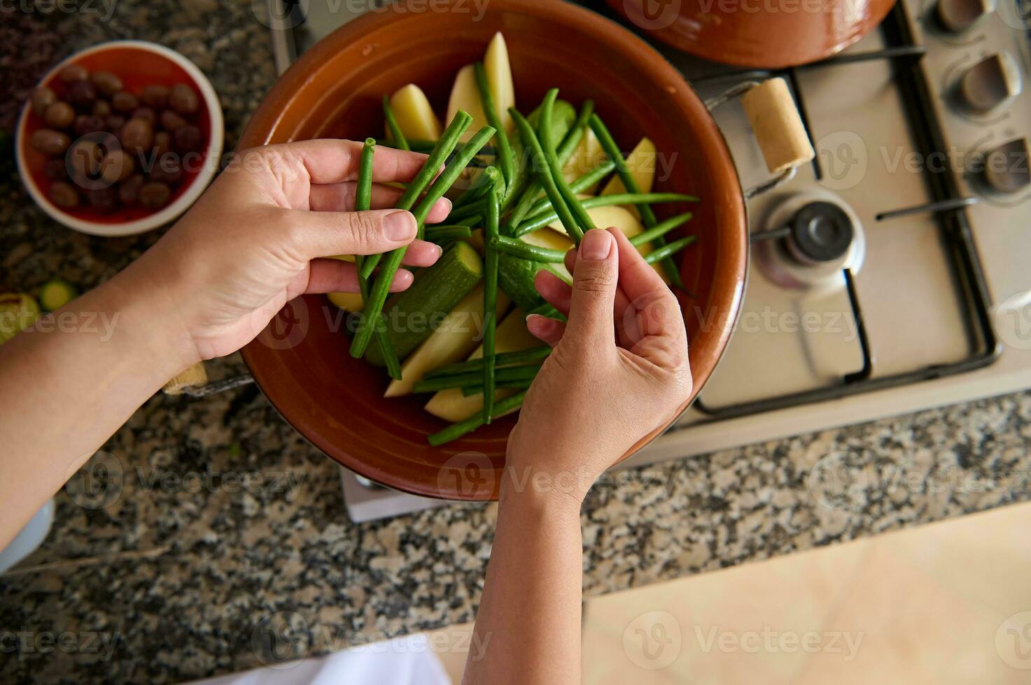 View from above of housewife hands putting fresh organic green beans on the tagine while cooking dinner in the kitchen photo